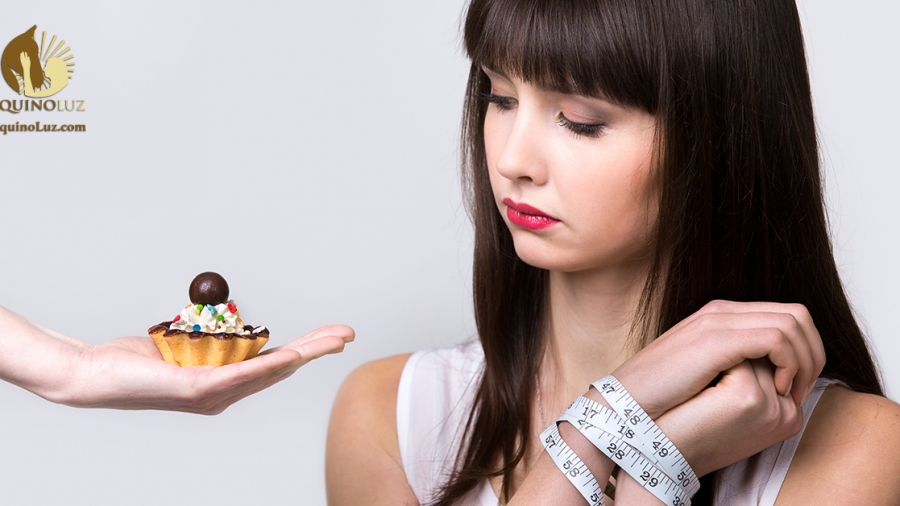 Young dieting woman sitting in front of delicious cream tart cake with hands tied with measuring tape, looking at forbidden food with longing and hungry expression, studio, gray background, isolated